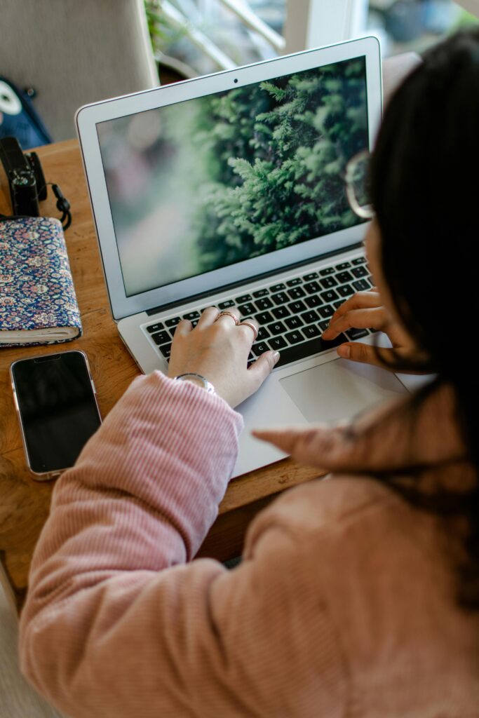 Woman blogging on MacBook with notepad and phone on desk